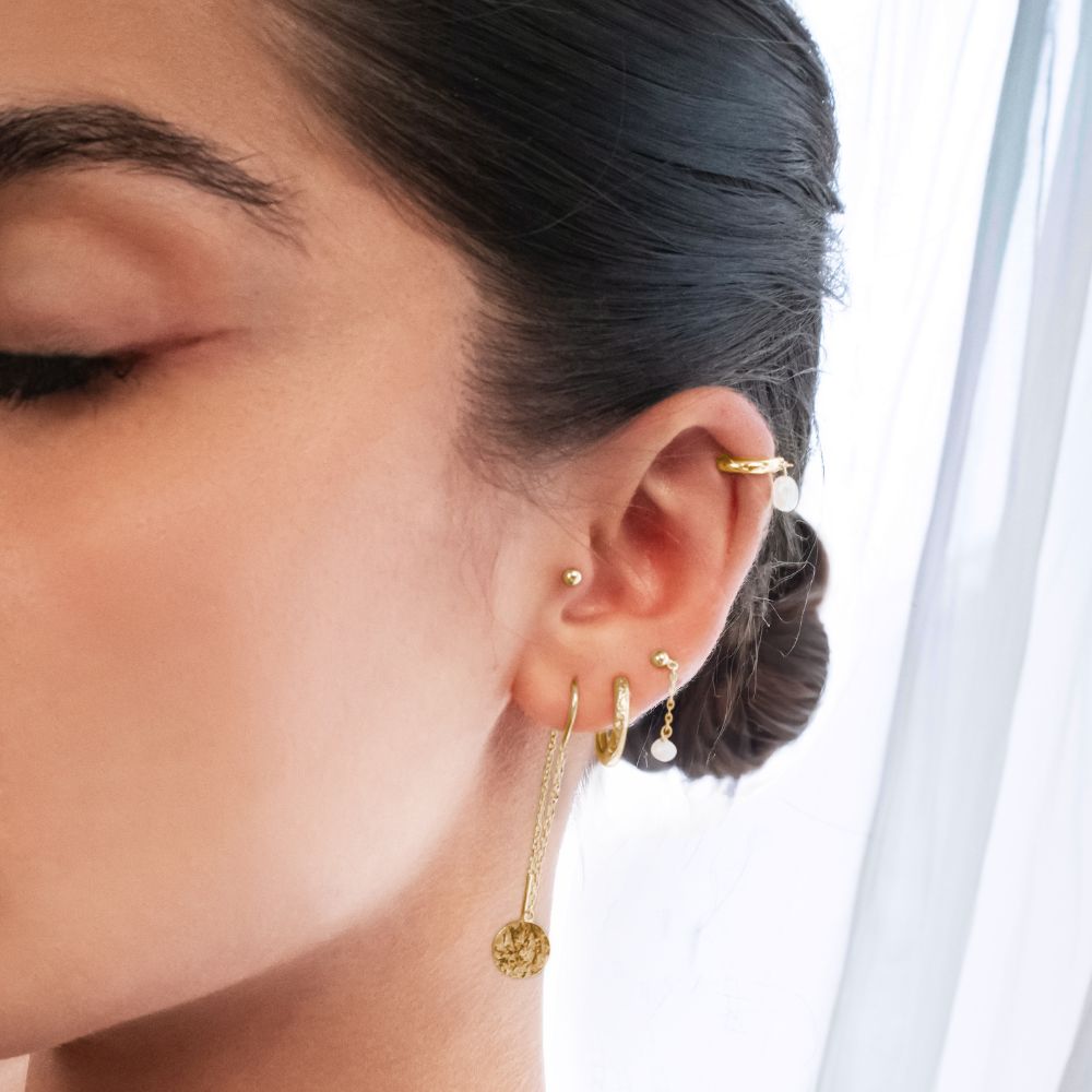 Close-up of a person wearing gold earrings with a neutral background