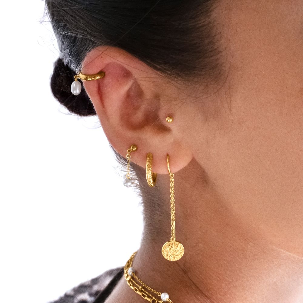 Close-up of an ear with gold earrings and a pearl earring on a neutral background